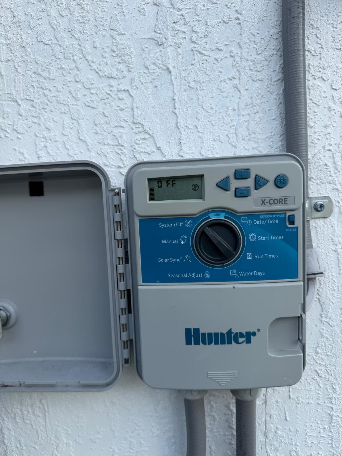 Hunter X-Core outdoor sprinkler timer mounted on a stucco wall with the controller door open.