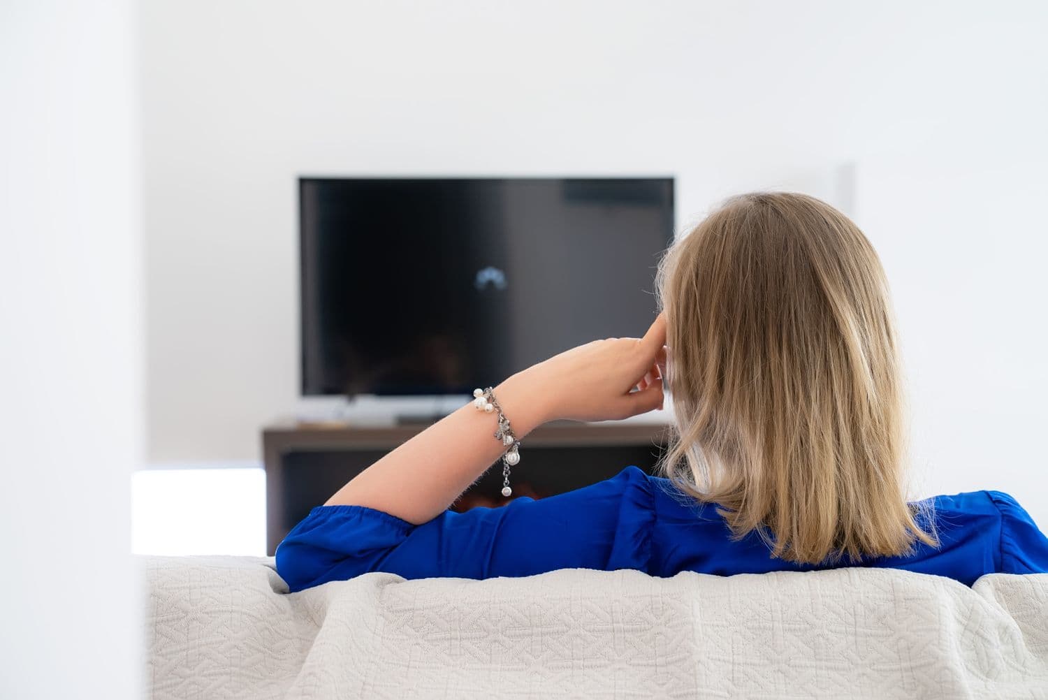 Woman sitting on a couch watching a buffering TV screen due to slow Wi-Fi connection at home
