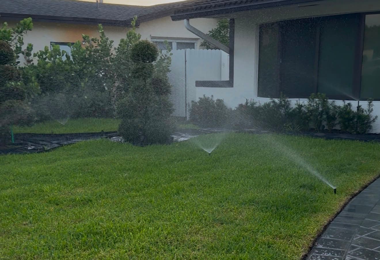 Residential sprinkler system watering a front lawn with multiple sprinkler heads providing irrigation coverage near a home