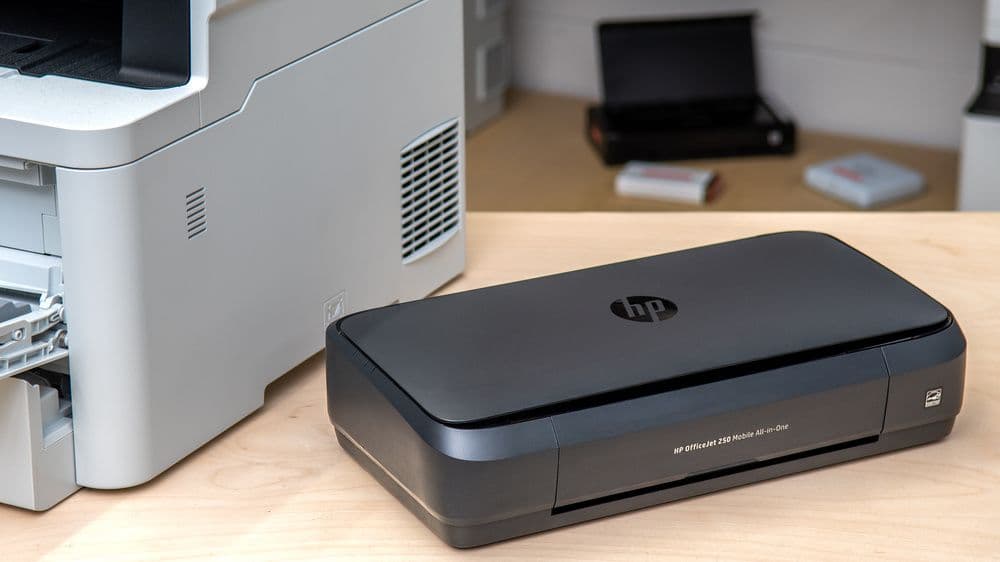Wireless office printer placed on a desk in an office workspace with another printer in the background.