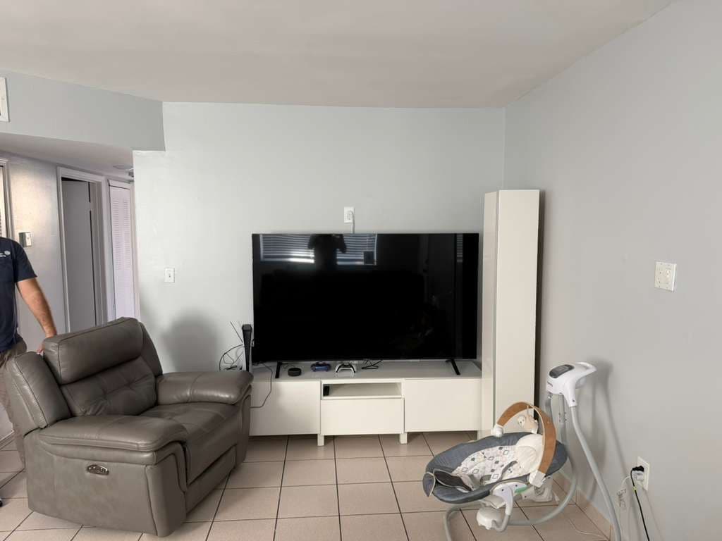 Before TV mounting service showing 75-inch TV on stand with visible cables in living room in Broward County