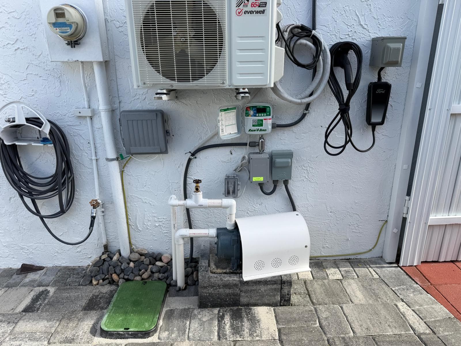 Newly installed sprinkler irrigation pump system with clean PVC piping, Rain Bird controller, and electrical connections on a South Florida home exterior wall in Miami.